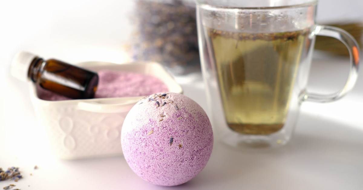13 Unique Small Gift Ideas for Teachers A lavender bathbomb next to a clear mug of tea. Behind the bathbomb and tea are lavender flowers.