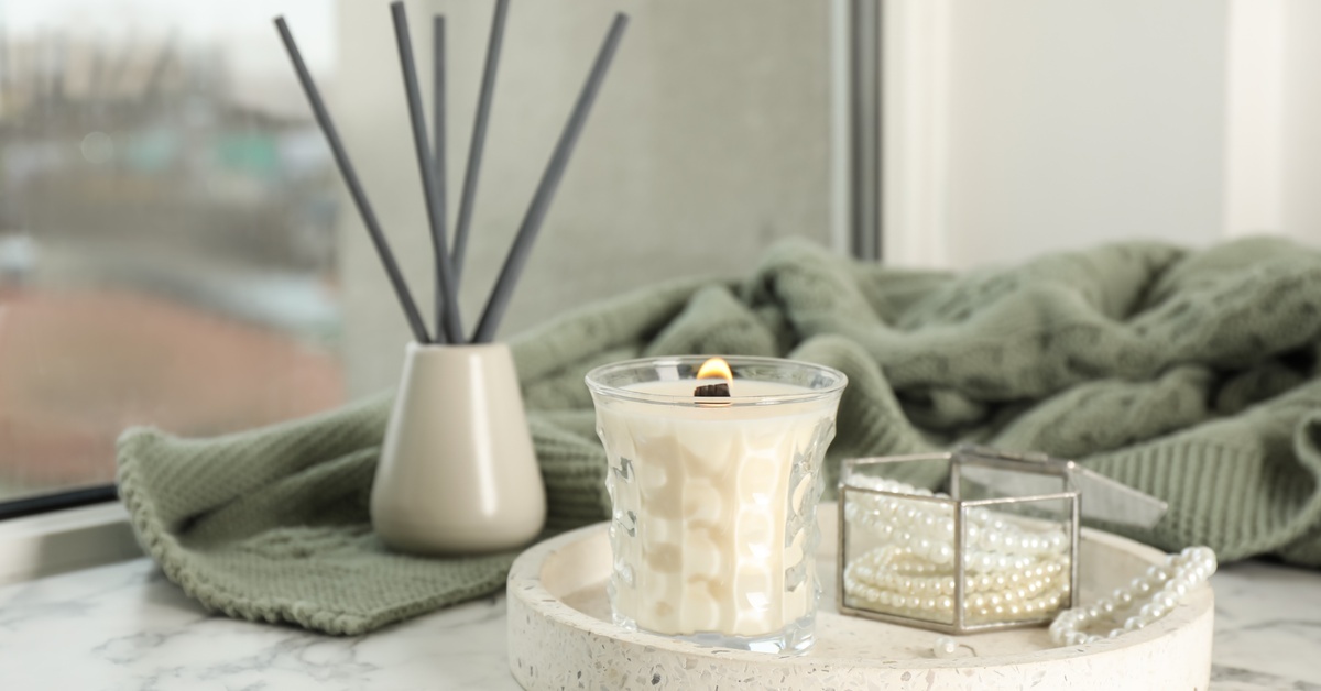 Creative Ways To Use a Trinket Tray in Your Home A close-up of a small, white tray on a dresser holding a glass jar with jewelry and a white burning candle.