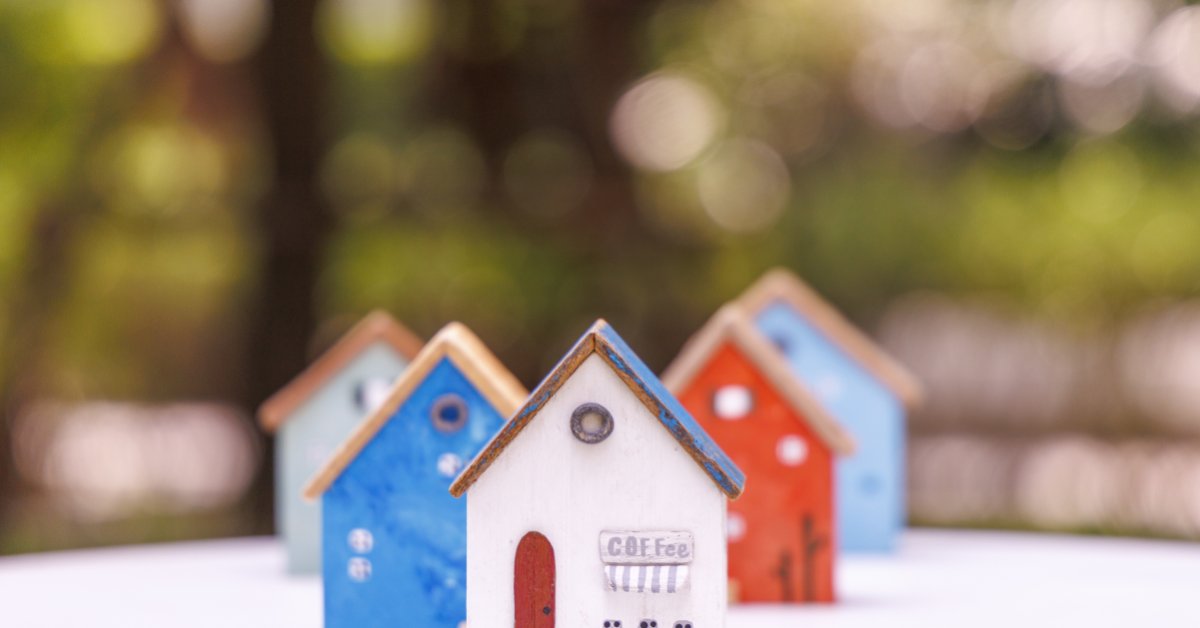 Miniature wooden houses in white, blue, pink, and yellow arranged on a white surface with green blur behind them.